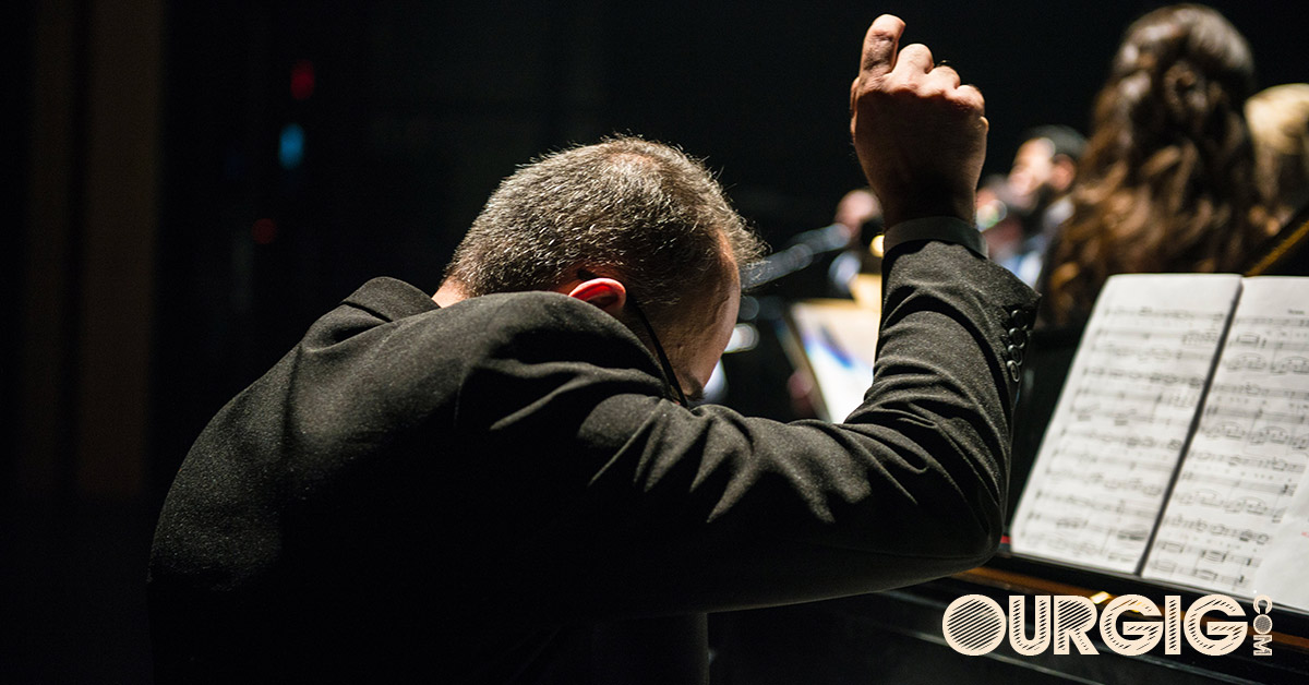 man directing an orchestra in concert ourgig.com