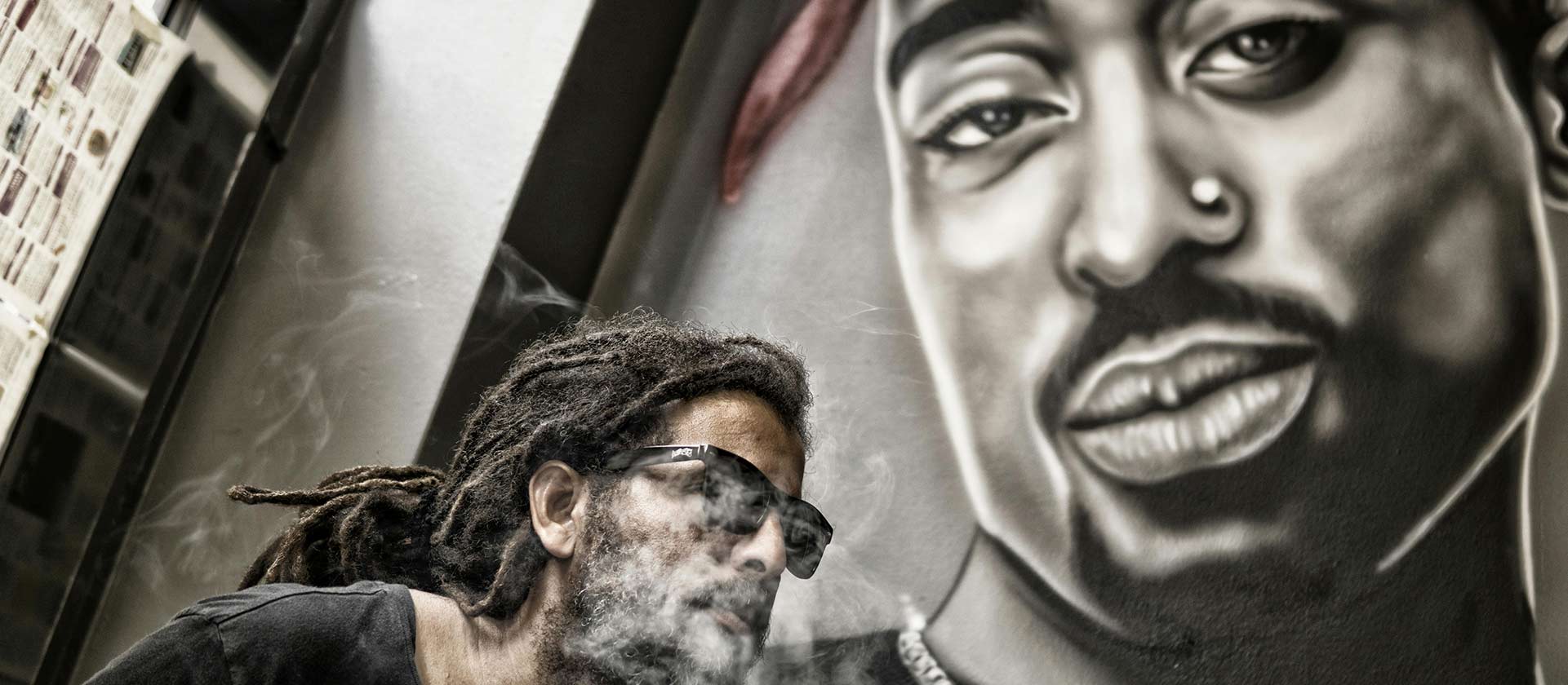 Man with dreadlocks standing in front of Tupac Shakur mural