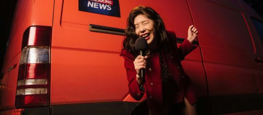 woman newscaster singing behind news van